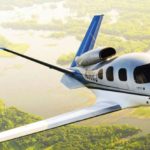 white and silver Cirrus jet flying over water and forest