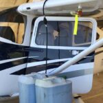 black and white Cessna 182 with two gas cans and the door open