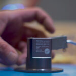 close-up of hard-anodized sender housing with a hand nearby